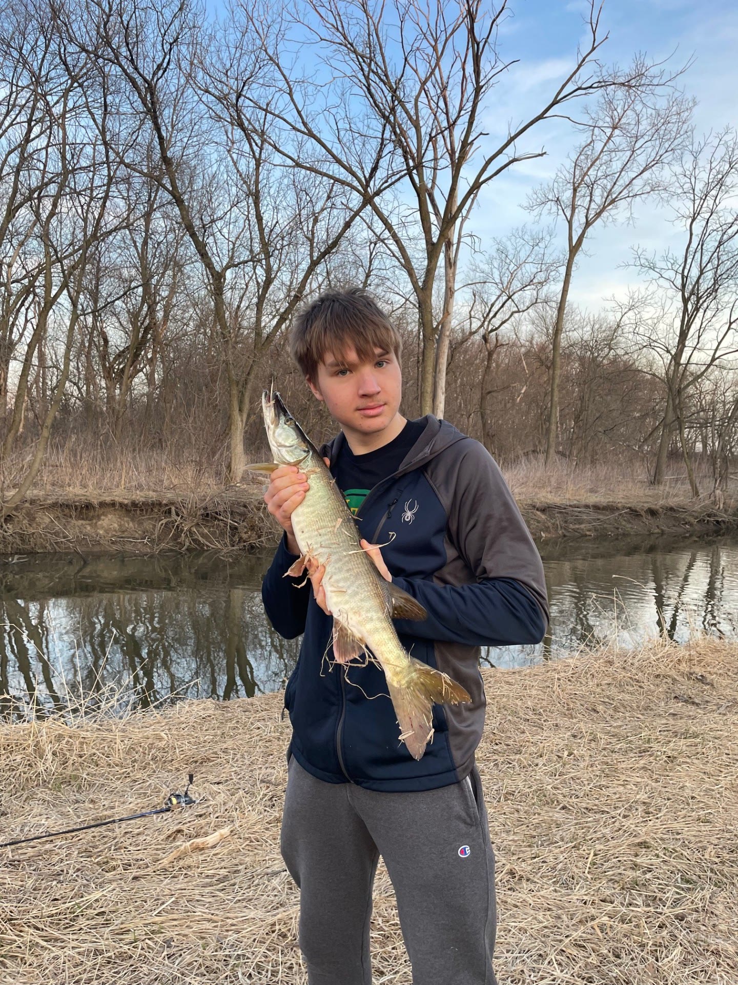 David holding a fish beside a wooded creek